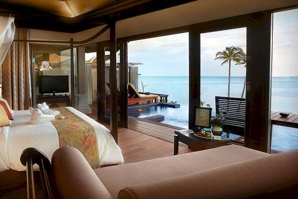 Innenansicht einer Hotelsuite mit Meerblick, Bett, Fernseher und offenem Balkon.
