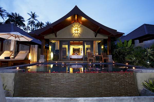 Außenansicht der Nora Buri Resort & Spa Villa bei Nacht mit Swimmingpool, Beleuchtung und Palmen.
