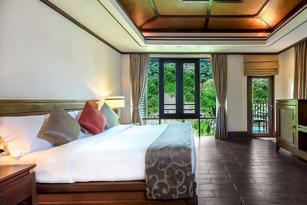 Schlafzimmer im Nora Buri Resort & Spa mit Bett, Kissen, Fernseher und Fenster mit Balkon.