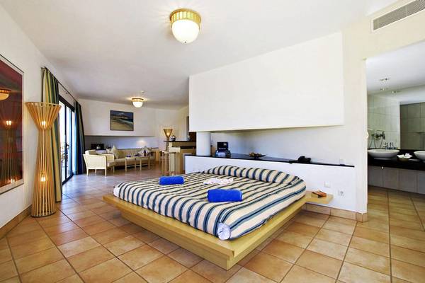 Schlafzimmer im Playitas Hotel mit Doppelbett, Holzboden und Badezimmer im Hintergrund.