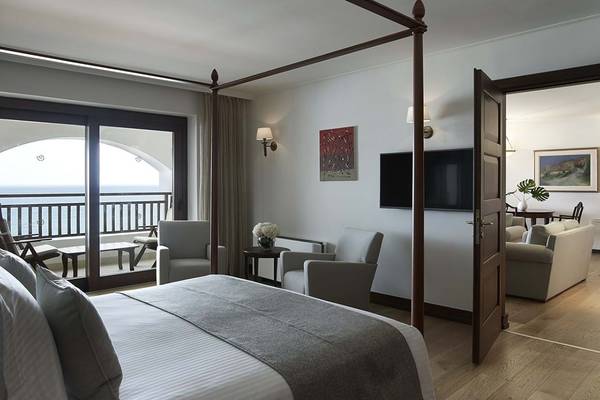 Hotelzimmer im Creta Maris Resort mit Blick auf das Meer, vier Posterbett, zwei Sessel, Fernseher und Balkon.