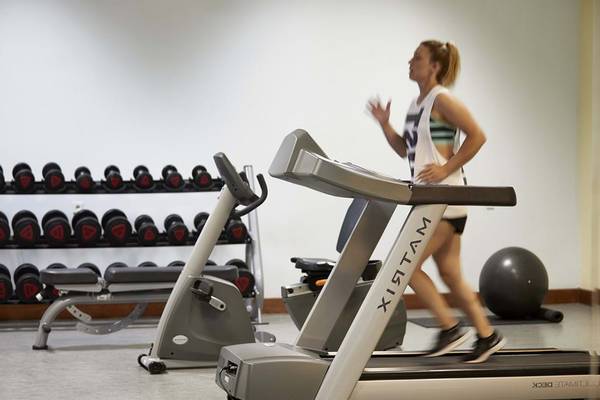 Frau im Fitnessstudio läuft auf einem Laufband vor einem Gewichtsregal und einer Yoga-Kugel.