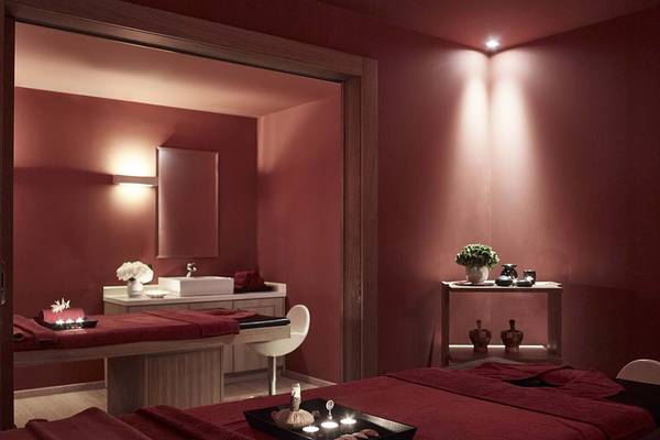 Spa-Behandlungsraum im Creta Maris Resort mit roten Wänden, zwei Behandlungstischen und einem weißen Stuhl.