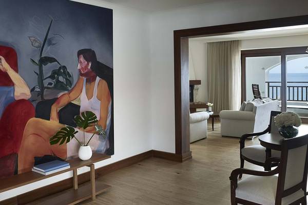 Innenansicht einer Hotelsuite mit großem Wandbild, Möbeln und Meerblick.