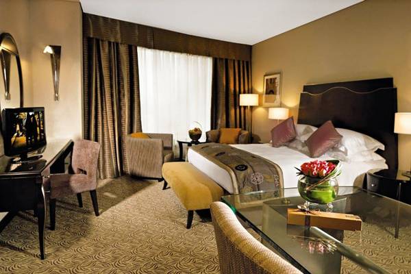 Rose Rayhaan by Rotana Hotelzimmer mit Bett, Schreibtisch und Wohnzimmermöbeln.