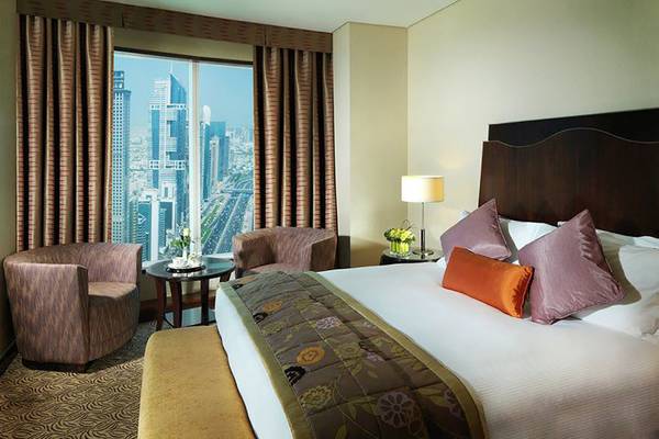 Rose Rayhaan by Rotana Hotelzimmer mit großem Bett, zwei Sesseln, und Panoramablick auf die Stadt.