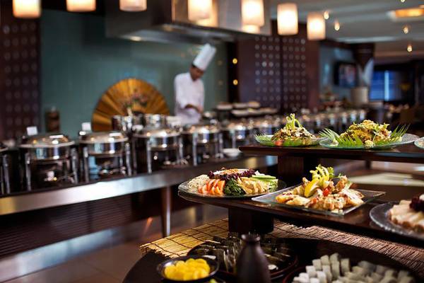 Buffettisch im Rose Rayhaan by Rotana Hotel mit verschiedenen Speisen und einem Koch im Hintergrund.