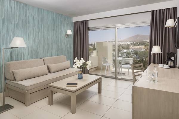 Innenansicht einer Suite im HD Beach Resort mit Wohnzimmer, Schlafsofa, Tisch, Blumenvase, Schreibtisch und Terrasse.