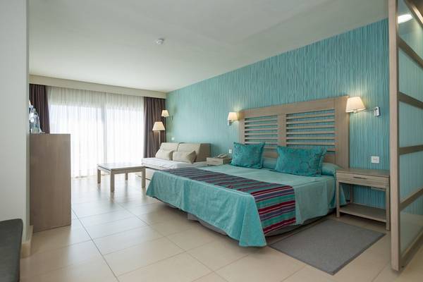 Innenansicht eines Hotelzimmers im HD Beach Resort mit blauen Wänden, einem Bett, einem Schreibtisch und einem Sofa.