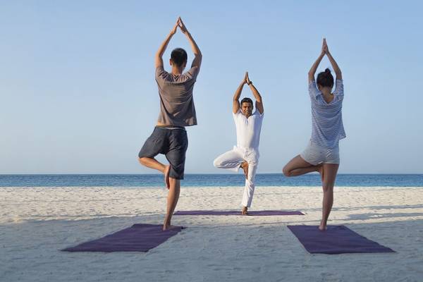 Drei Personen machen Yoga auf dem Strand des Komandoo Island Resorts & Spa.