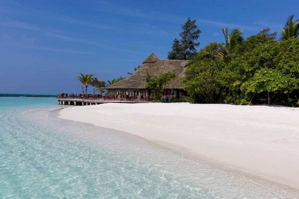 Strand des Komandoo Island Resort & Spa mit baumbewachsener Insel im Hintergrund.