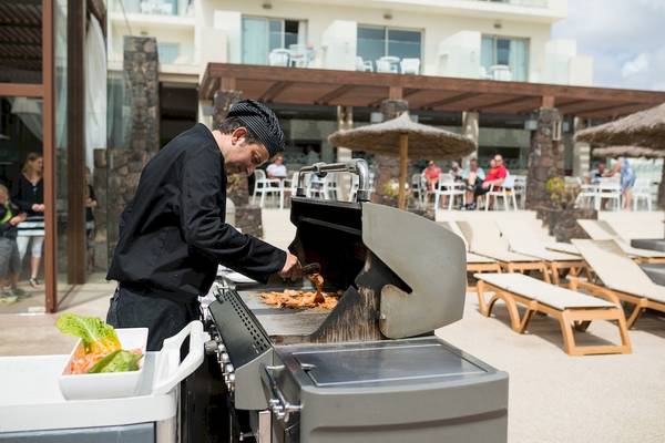 Grill-Mitarbeiter im HD Beach Resort, der vor Gästen grillt, mit Gästen und Sonnenliegen im Hintergrund.
