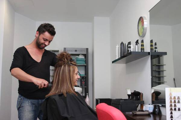 Ein Mann, der in einem Salon eine Kundin frisiert, während sie in einem roten Stuhl sitzt.