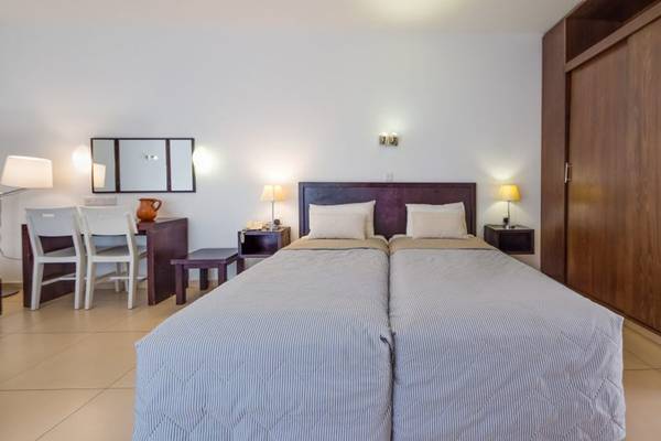 Innenansicht eines Doppelzimmers im Callisto Holiday Village mit zwei Betten, Nachttischen und einer Lampe.