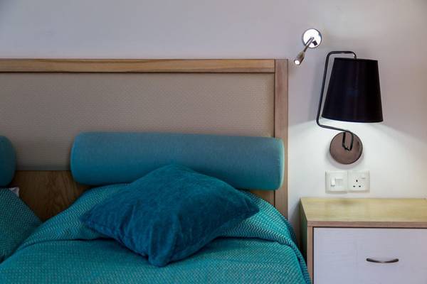 Ein Bett mit blauen Kissen und einer Wandlampe im Schlafzimmer des Callisto Holiday Village.
