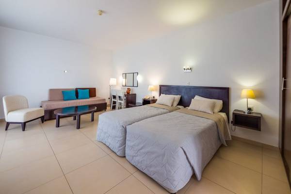 Schlafzimmer im Callisto Holiday Village mit zwei Betten, Nachttischen, Lampen und einem Sofa.