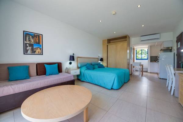 Innenansicht eines Zimmers im Callisto Holiday Village mit einem Bett, einem Sofa, einem Tisch und einer Küche.