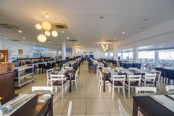 Restaurant des Callisto Holiday Village mit vielen Tischen und Stühlen, beleuchtet von Hängelampen.