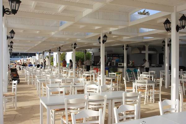 Restaurant im Callisto Holiday Village mit vielen weißen Tischen und Stühlen unter einem Überdach.