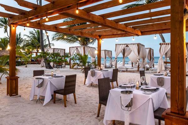 Außenbereich eines Strandrestaurants im Sunscape Coco Punta Cana Hotel mit beleuchteten Sonnensegeln und gedeckten Tischen.