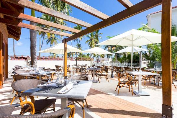 Terrasse des Sunscape Coco Punta Cana Hotels mit mehreren Tischen und Stühlen, überdacht von großen weißen Sonnenschirmen.