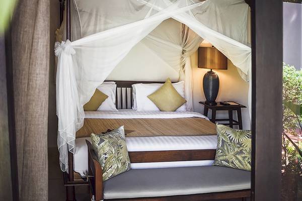 Bett mit Baldachin im Saree Samui Resort mit Kissen, Lampe und Tageslicht.