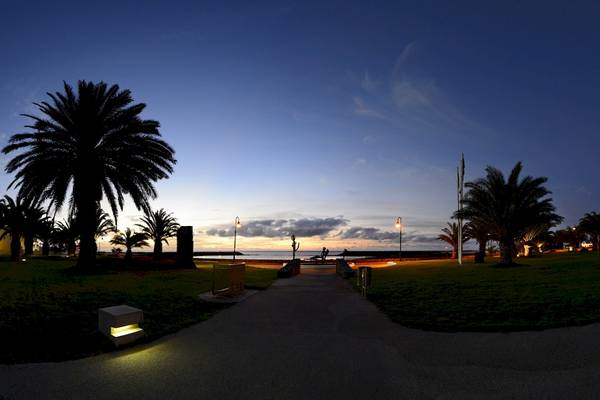 Außenbereich des HD Beach Resorts bei Sonnenuntergang mit Palmen und einem Weg, der zum Meer führt.