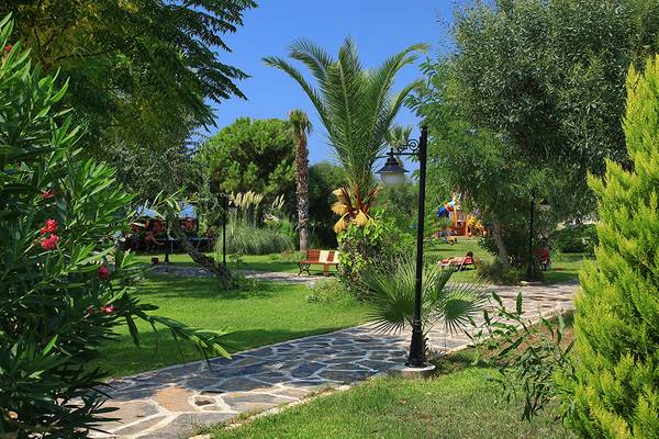 Garten des Club Yali Hotels & Resort mit gepflastertem Weg, Palmen und einem Sonnenschirm.