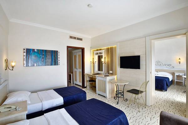 Doppelzimmer im Club Yali Hotels & Resort mit zwei Betten, Fernseher, Schreibtisch und Badezimmereingang.