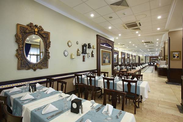 Innenansicht des Restaurants im Club Yali Hotels & Resort mit gedeckten Tischen und dekorativen Wanduhren.