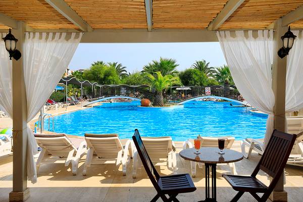 Aussicht auf den Poolbereich des Club Yali Hotels & Resorts mit Sonnenliegen und einem Tisch mit Getränken.