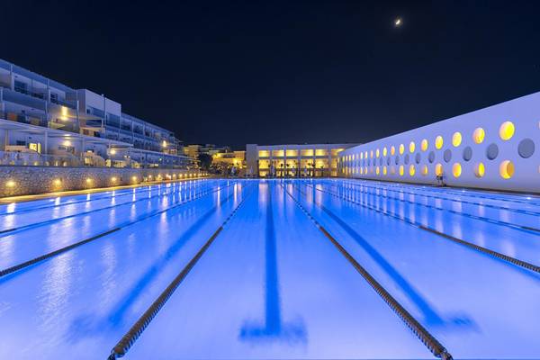 Nachtansicht des Lyttos Beach Hotel Schwimmbads, beleuchtet und mit Gebäuden im Hintergrund.