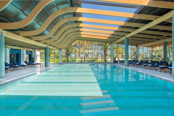 Schwimmbad des Lyttos Beach Hotels mit Sonnenliegen und Glaswänden