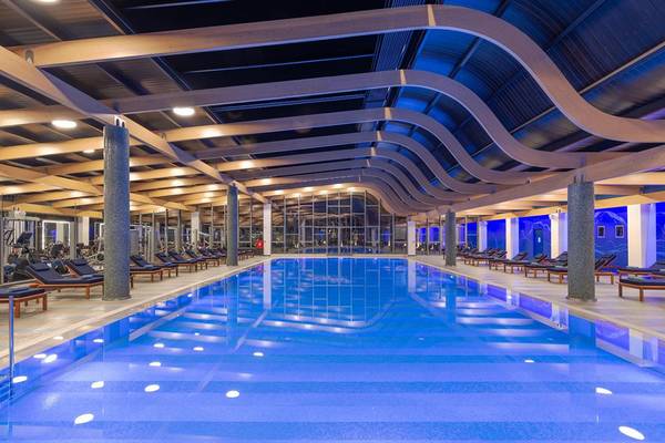 Innenpool des Lyttos Beach Hotels mit Loungeliegen und Fitnessgeräten.