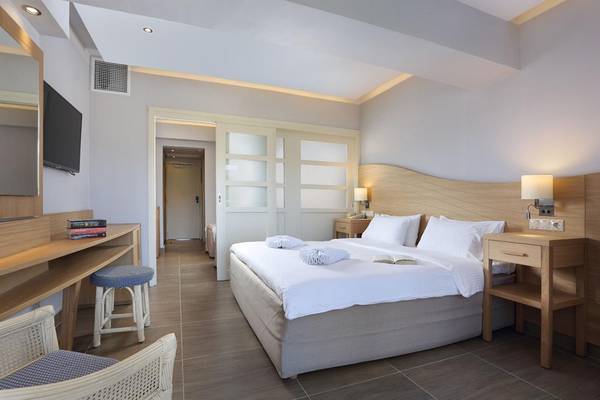 Innenansicht eines Zimmers im Lyttos Beach Hotel mit einem Bett, Nachttischen und Möbeln.