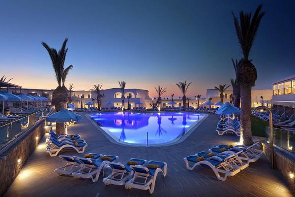 Der beleuchtete Poolbereich des Lyttos Beach Hotels bei Nacht mit Lounge-Liegestühlen und Sonnenschirmen.