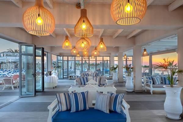 Lounge-Bereich des Lyttos Beach Hotels mit blauen und weißen Kissen, Holzlampen und Blick auf den Sonnenuntergang.