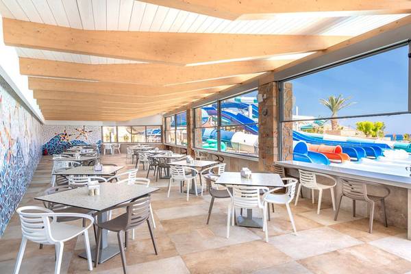 Innenansicht des Restaurants im Lyttos Beach Hotel mit Tischen und Stühlen, Wasserrutschen im Hintergrund.
