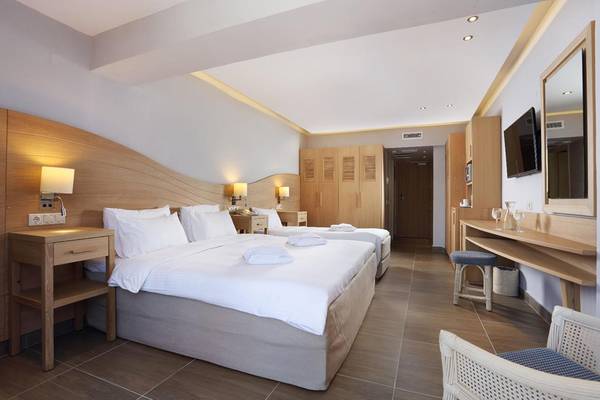 Innenansicht eines Doppelzimmers im Lyttos Beach Hotel mit zwei Betten, Nachttischen, Kleiderschränken und einem Fernseher.