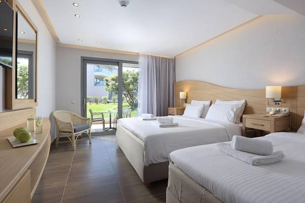 Innenansicht eines Doppelzimmers im Lyttos Beach Hotel mit zwei Betten, Tisch, Sessel und Terrasse.