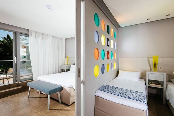 Innenansicht eines Zimmers im Lyttos Beach Hotel mit zwei Betten, einem gemusterten Wandpaneel und einer Terrassentür.