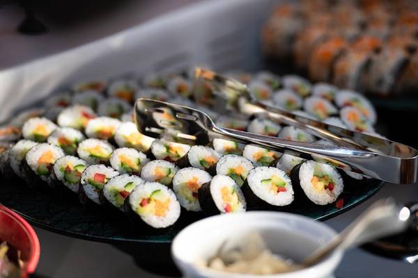 Ein Teller mit verschiedenen Sushi-Rollen, serviert mit Zange und einer Schüssel Sojasauce.