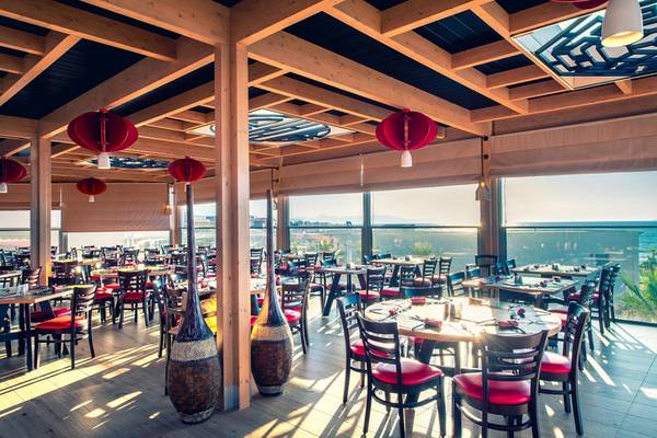 Innenansicht des Restaurants im Lyttos Beach Hotel mit vielen Tischen und Stühlen, roten Laternen und Glaswänden.