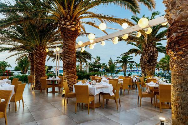 Außenbereich des Lyttos Beach Hotels mit gesäumten Tischen und Palmen.