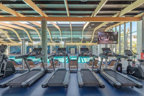 Fitnesscenter im Lyttos Beach Hotel mit mehreren Laufbändern und Blick auf den Pool.