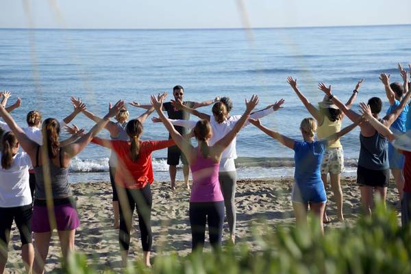 Gruppe von Menschen, die Yoga am Strand mit einem Trainer praktizieren
