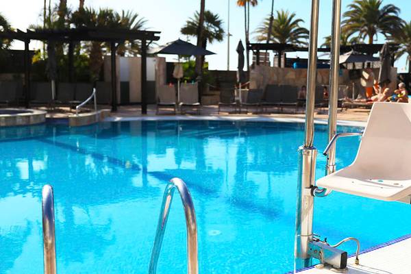 Ein behindertengerechter Stuhl steht am Rande des Schwimmbeckens im Corallium Dunamar Garden by Lopesan Hotels.