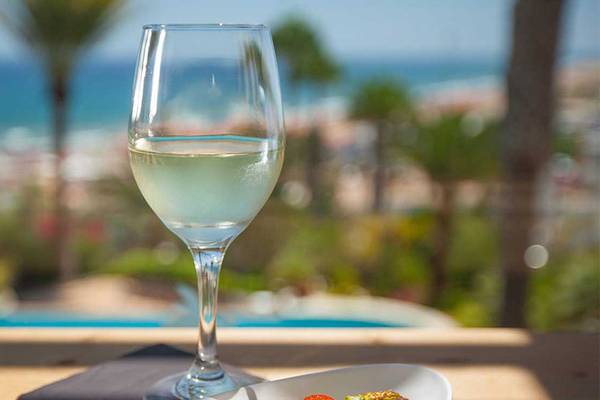 Ein Glas weißer Wein mit Blick auf das Meer und einen Pool