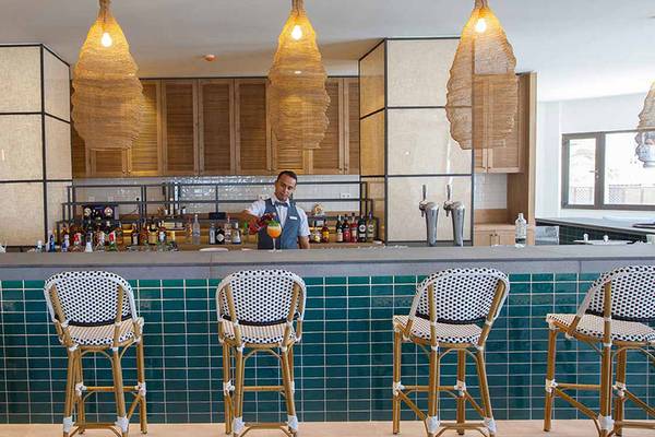 Die Bar im Corallium Dunamar Garden by Lopesan Hotels mit einem Barkeeper, der Getränke zubereitet.
