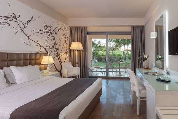 Ein modernes Hotelzimmer im Princess Andriana Resort & Spa mit einem Bett, Schreibtisch, Fernseher und Gartenblick.